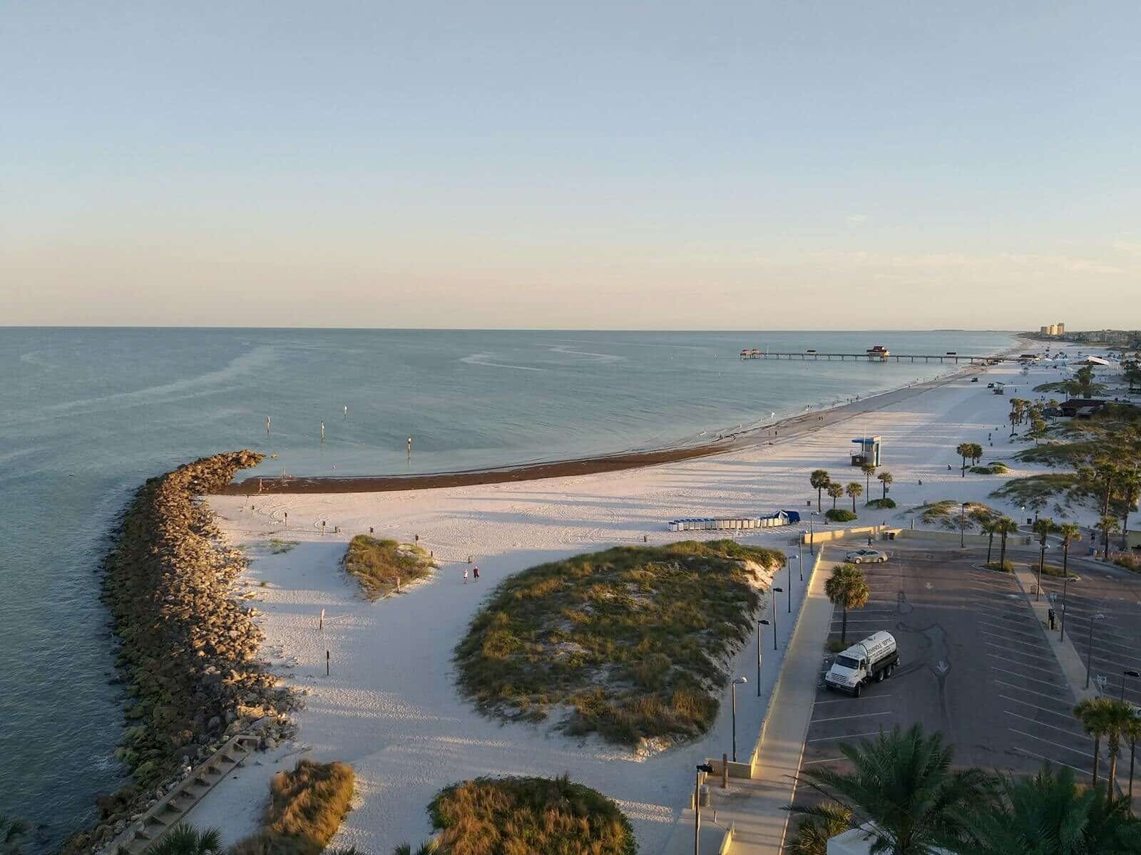 Stunning aerial view of a sandy beach with a pier at sunset, showcasing the tranquil seaside atmosphere.