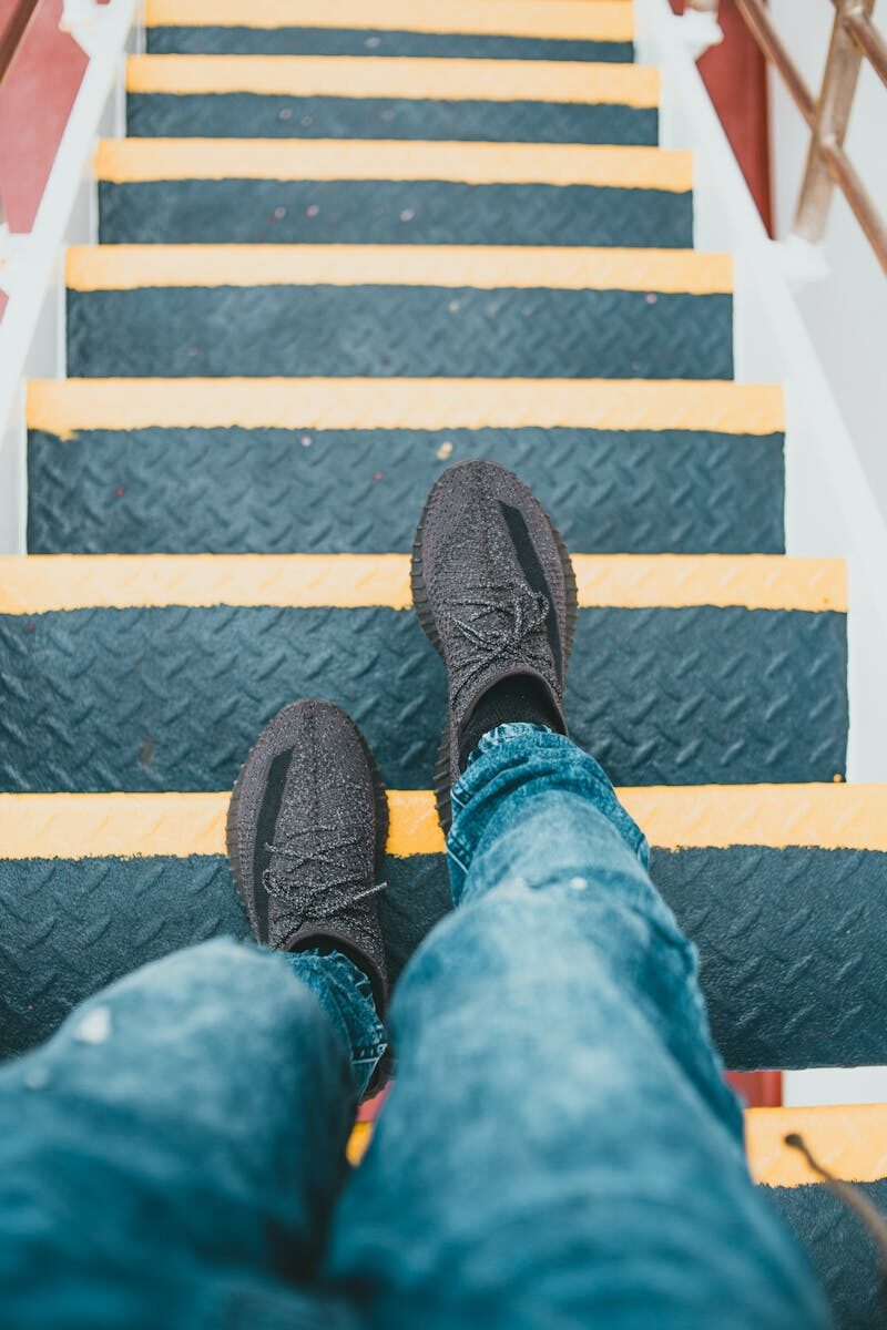 A person's feet in sneakers taking a step down outdoor stairs with yellow stripes.