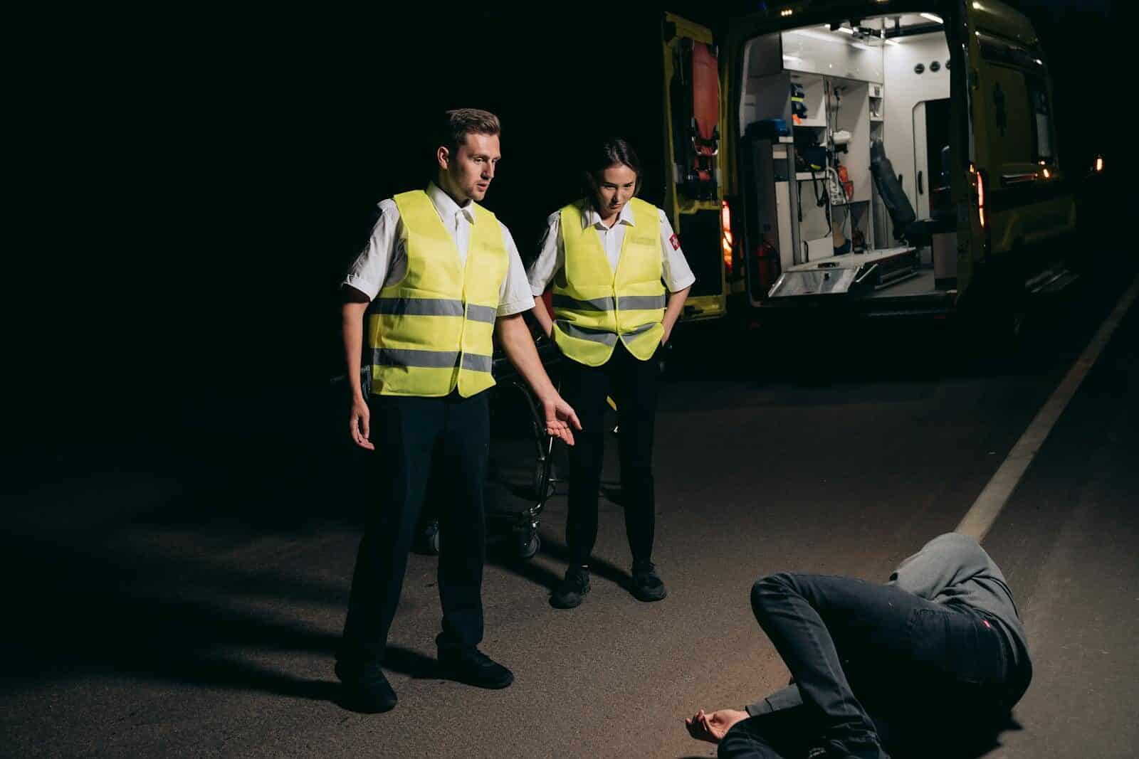 Paramedics assist a patient on a dimly lit street, showcasing emergency response at night.
