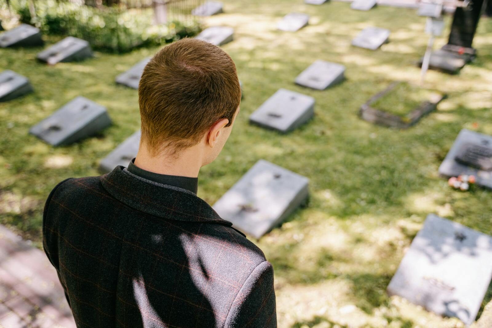 A man stands in contemplation at a serene memorial park surrounded by tombstones.